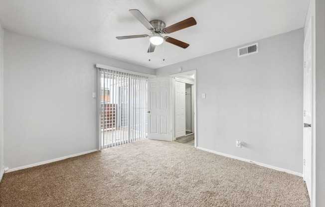 an empty living room with a ceiling fan and a door to a balcony