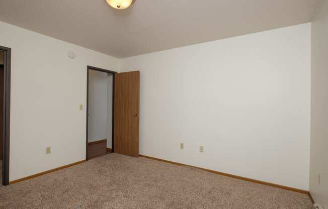 a bedroom with carpet and a door to a closet. Fargo, ND Park Circle Apartments.