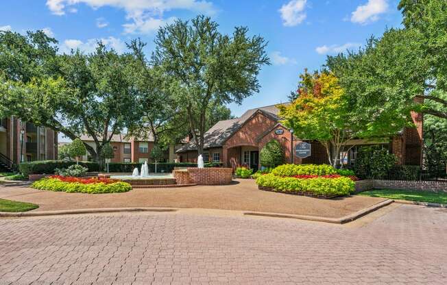 a fountain sits in front of a brick building with trees in the background