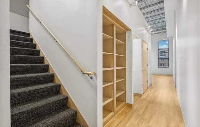 A staircase with a wooden handrail and steps covered in a textured carpet leads up to a doorway.