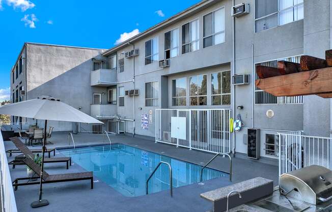 A pool area with a grill and lounge chairs.
