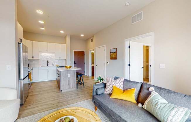 a living room and kitchen with a grey couch and yellow pillows