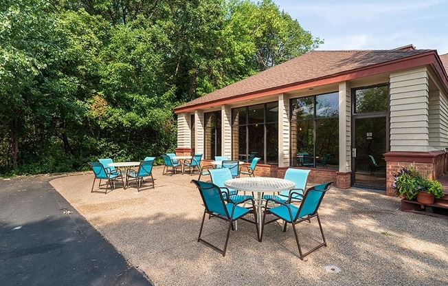 Outdoor patio with blue chairs and round tables in front of the indoor pool building