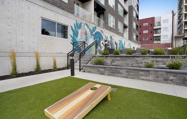 A wooden bench sits on a green lawn in front of a building with a mural.