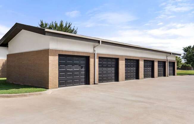 A building with a brown brick facade and a white roof has six black garage doors.