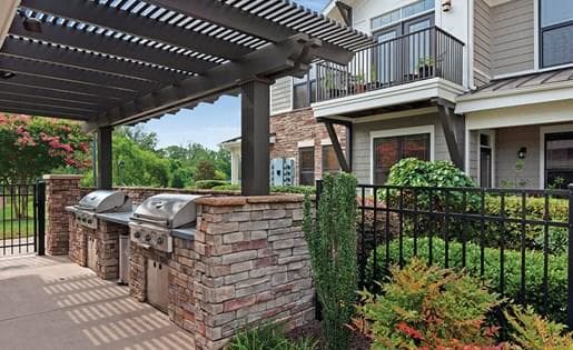 outdoor kitchen covered by pergola housing two large stainless steel gas grills set with stone counter tops and accents