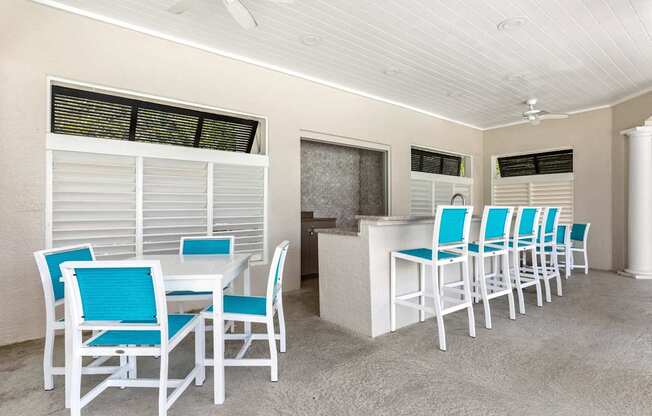 A white table with blue chairs is in a room with a ceiling fan.