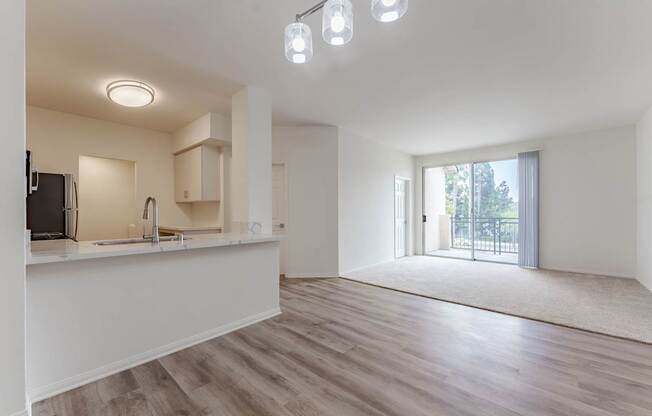 A spacious, empty room with a kitchen area and a door leading to a balcony.