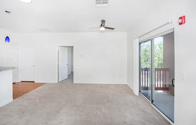 A spacious room with a ceiling fan and sliding glass doors leading to a balcony.