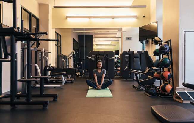 a woman sitting on a yoga mat in a gym