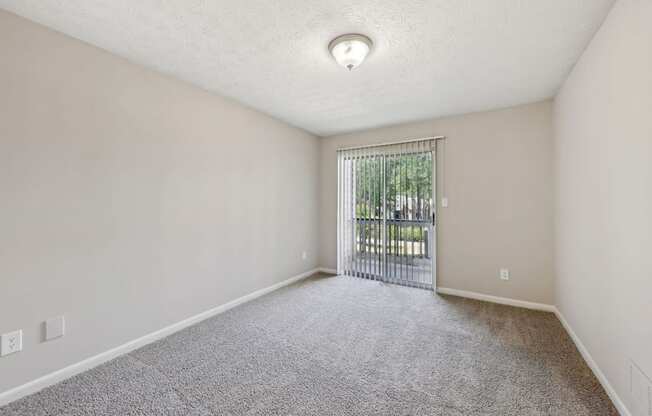 A room with a carpeted floor and a sliding glass door leading to a balcony at Gwinnett Square Apartments in Duluth, GA