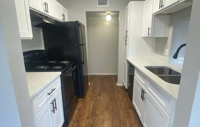 a kitchen with white cabinets and black appliances and a wood floor