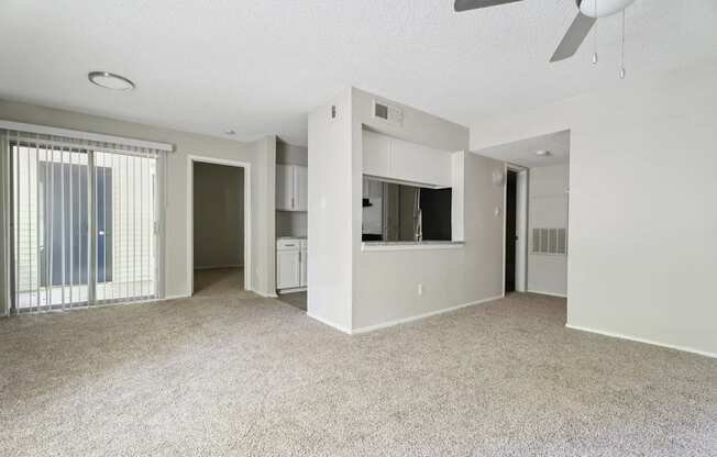 A spacious living room with a ceiling fan and carpeted floor.