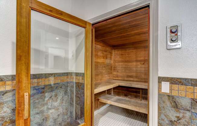 A wooden door with a glass window is open to a bathroom with a bench.