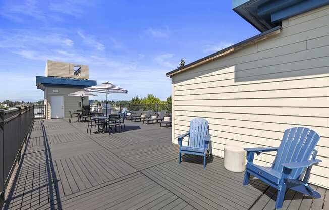 a large Rooftop Resident Lounge deck with blue Adirondack chairs and umbrellas at Guinevere Apartment Homes, Washington, 98103