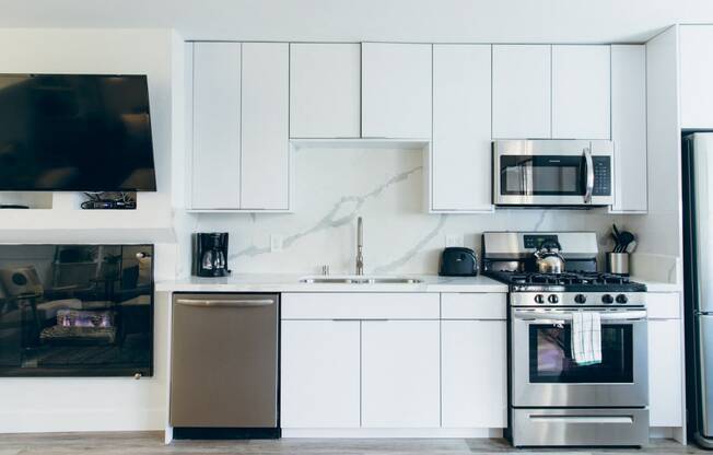 Kitchen with stainless steel dishwasher, gas range, micro hood microwave, single kitchen sink, backsplash and countertops, white kitchen cabinets, cozy fireplace on the left