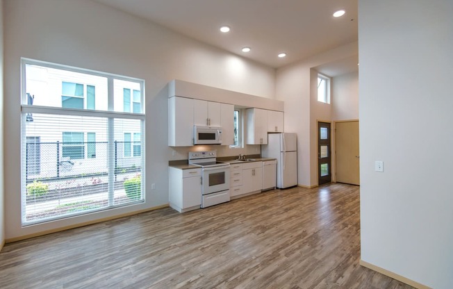 an empty living room with a kitchen and a large window