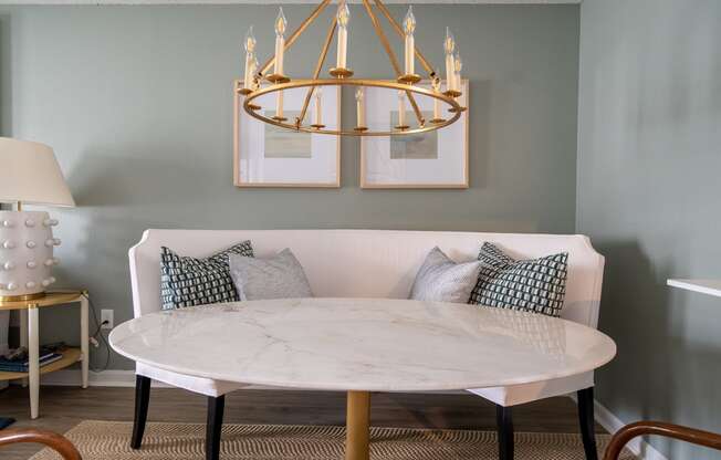 a round marble table with pillows on it under a brass chandelier