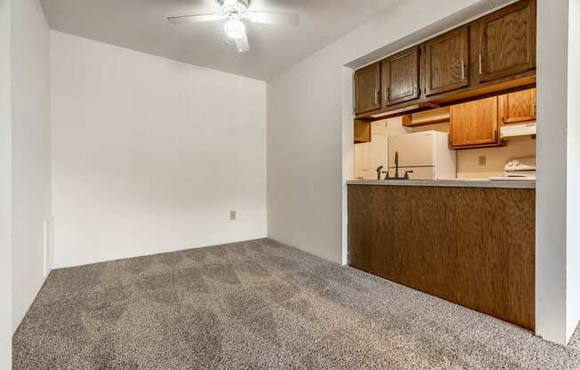 A room with a carpeted floor and a kitchen area in the background