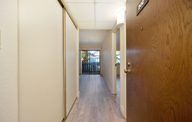 a hallway with a wooden door leading to a room with a balcony