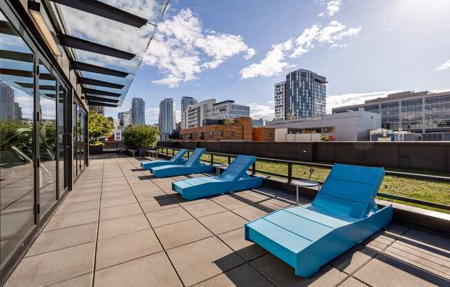 an outdoor deck with blue lounge chairs and a city skyline in the background