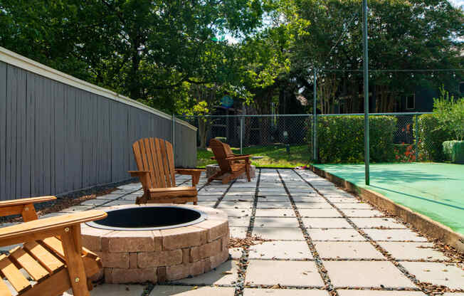 a patio with a fire pit and chairs next to a tennis court