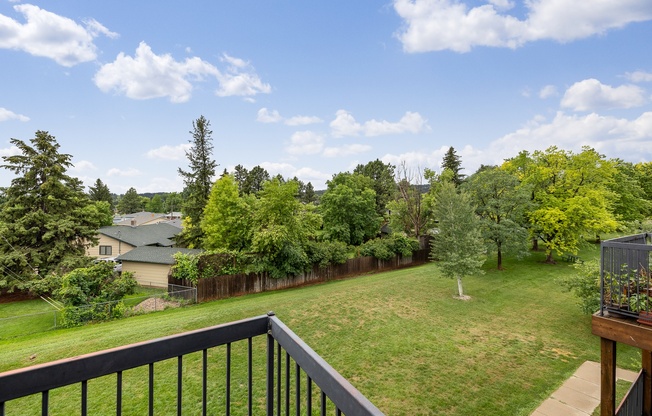 A balcony overlooks a green yard with trees.