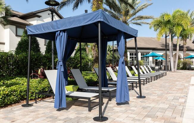 a row of lounge chairs under a blue gazebo with umbrellas