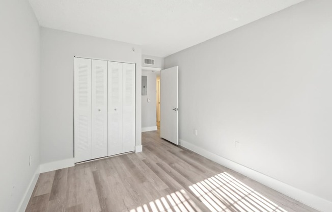 A room with white walls and a wooden floor with sunlight coming through the window.