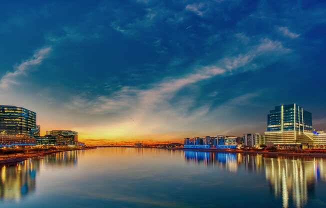 A cityscape at dusk with buildings reflecting in the water.