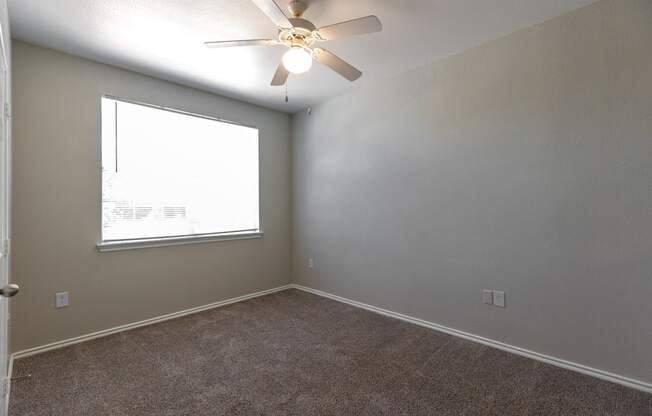 an empty bedroom with a ceiling fan and a window