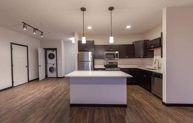 A modern kitchen here at The Park featuring dark wood cabinets, stainless steel appliances, large island, and open layout with in-unit laundry nearby, creating a stylish, spacious, and convenient living space.