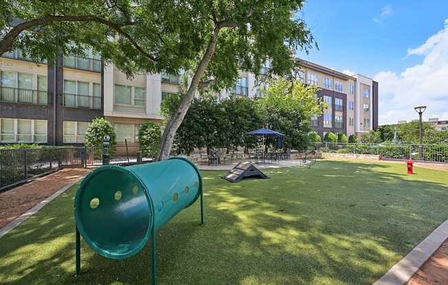 A playground with a green slide and a tent in the background.