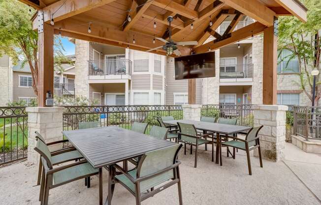 a patio with tables and chairs and a wooden gazebo with a television