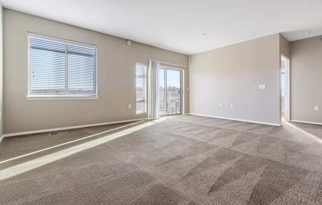 A large, empty room with carpeted flooring and a window with blinds.