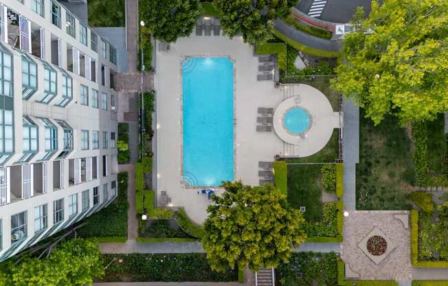 An aerial view of a pool surrounded by a building and trees.