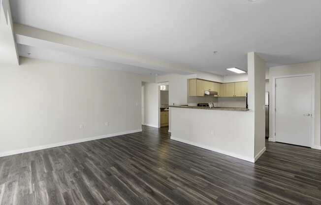 Unfurnished living room with plank flooring, tall ceilings, and a kitchen in the background at Arabella Apartment Homes, Washington, 98155