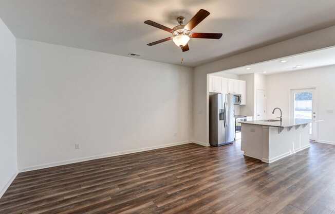an empty living room with a kitchen and a ceiling fan