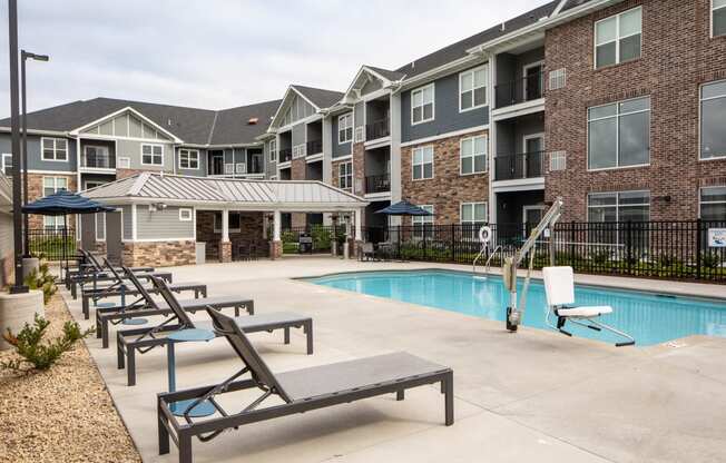 a swimming pool with chaise lounge chairs and umbrellas in front of an apartment building