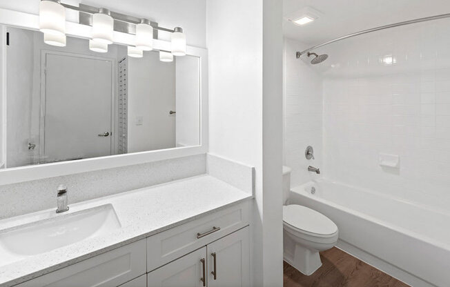 A white bathroom with a sink, mirror, toilet and bathtub.
