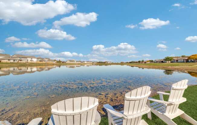 two white chairs sitting on the grass near a lake