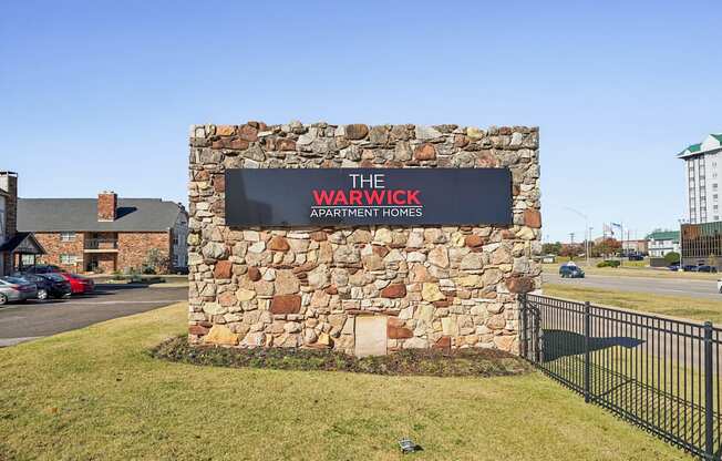 A stone wall with a sign that says "The Warwick Apartment Homes".