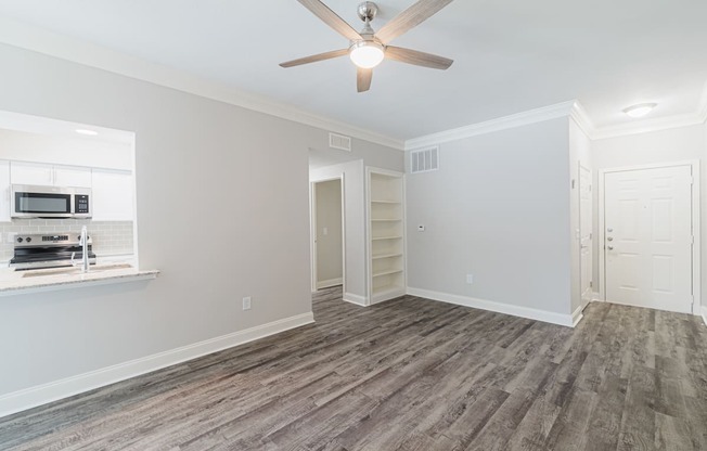 an empty living room with a ceiling fan and a kitchen