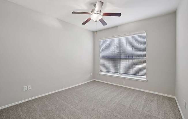 A room with a ceiling fan and a window with blinds.