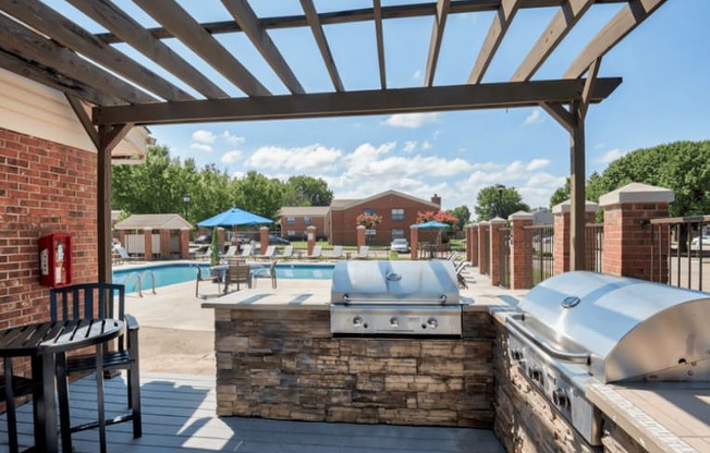 a patio with a grill and a swimming pool with umbrellas at Brightwaters Apartments, Little Rock, AR