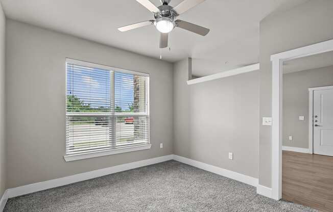 an empty bedroom with a ceiling fan and a window