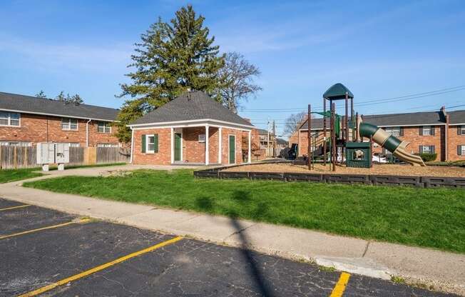 a playground sits in the middle of a grassy area in front of a brick building