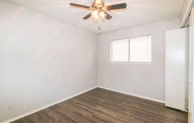 an empty bedroom with a ceiling fan and a window