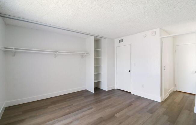 A room with white walls and wooden flooring with a closet and a door.
