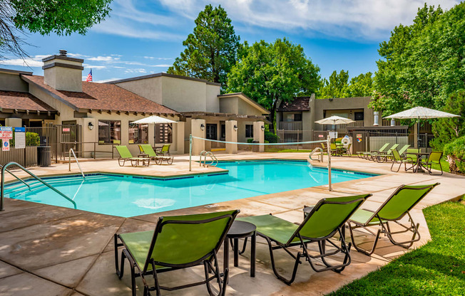 A pool surrounded by lawn chairs and trees.